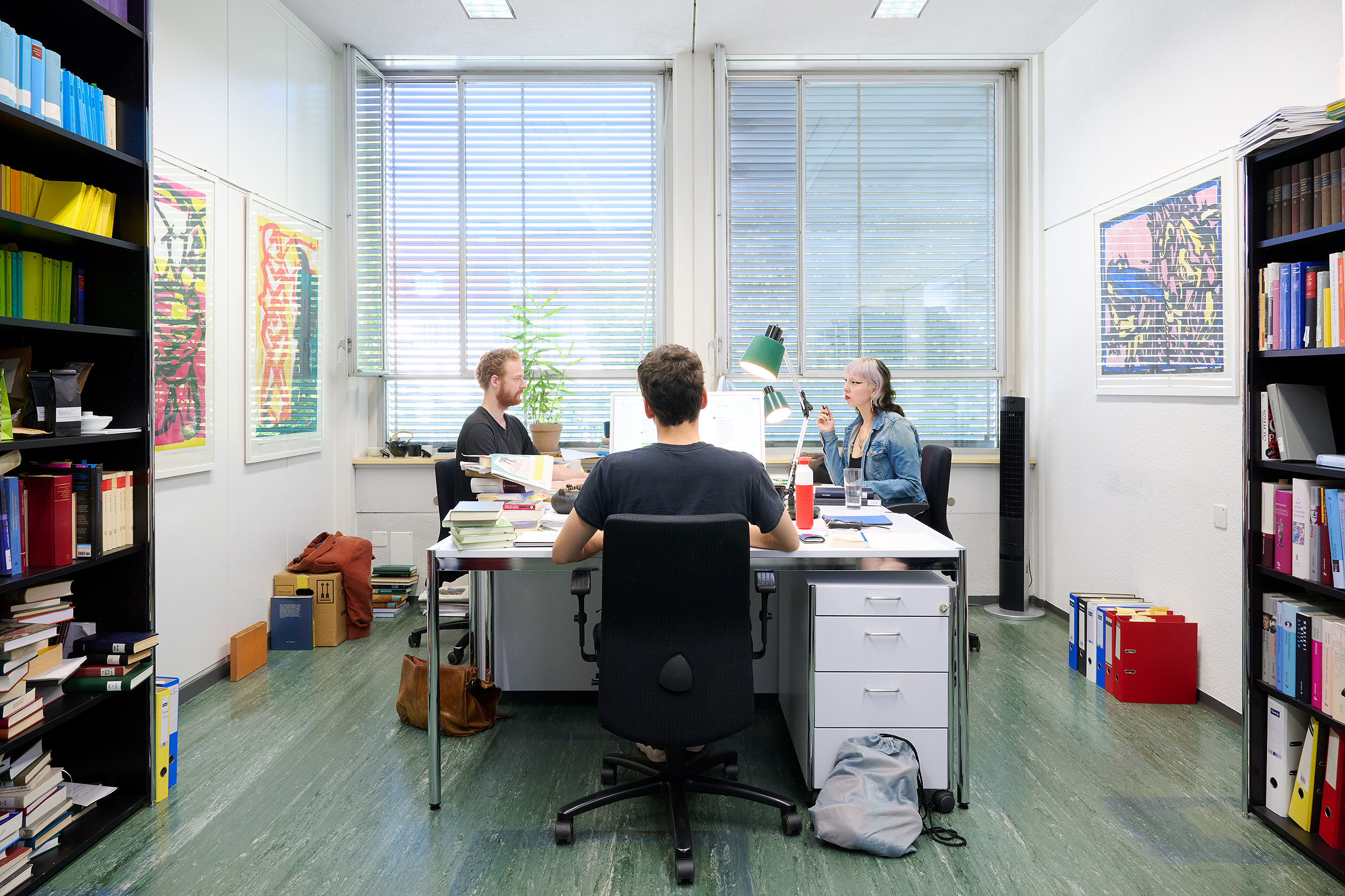 Das Foto zeigt eine Doktorandin an ihrem Arbeitsplatz. An der Wand hängt ein Plakat zu 100 Jahre Tove Jansson, auf dem Tisch liegen Bücher.