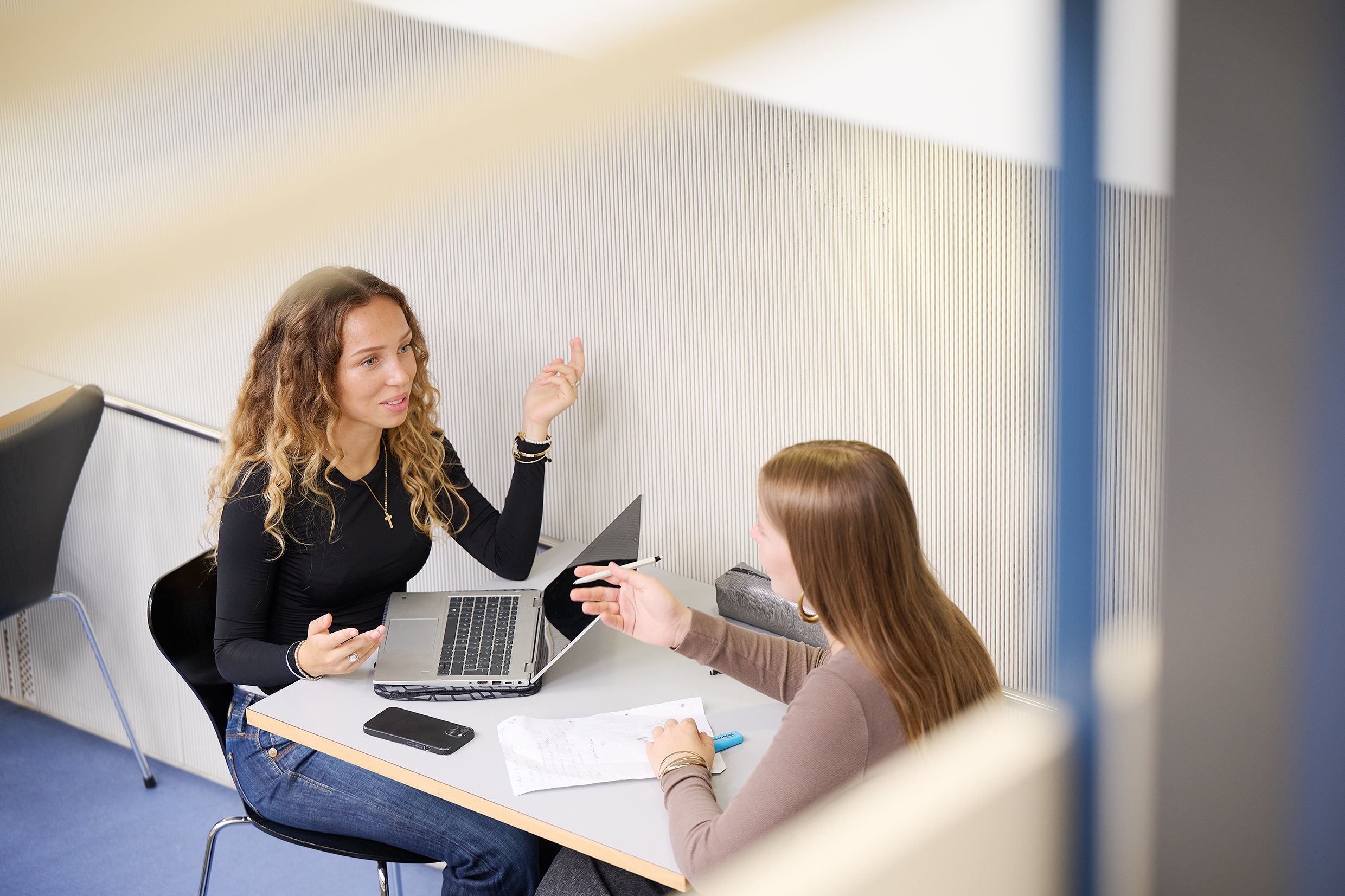 Das Bild zeigt eine Gruppe von Studierenden, die vor einem grün-roten Gebäude der Universität lebhaft diskutieren.