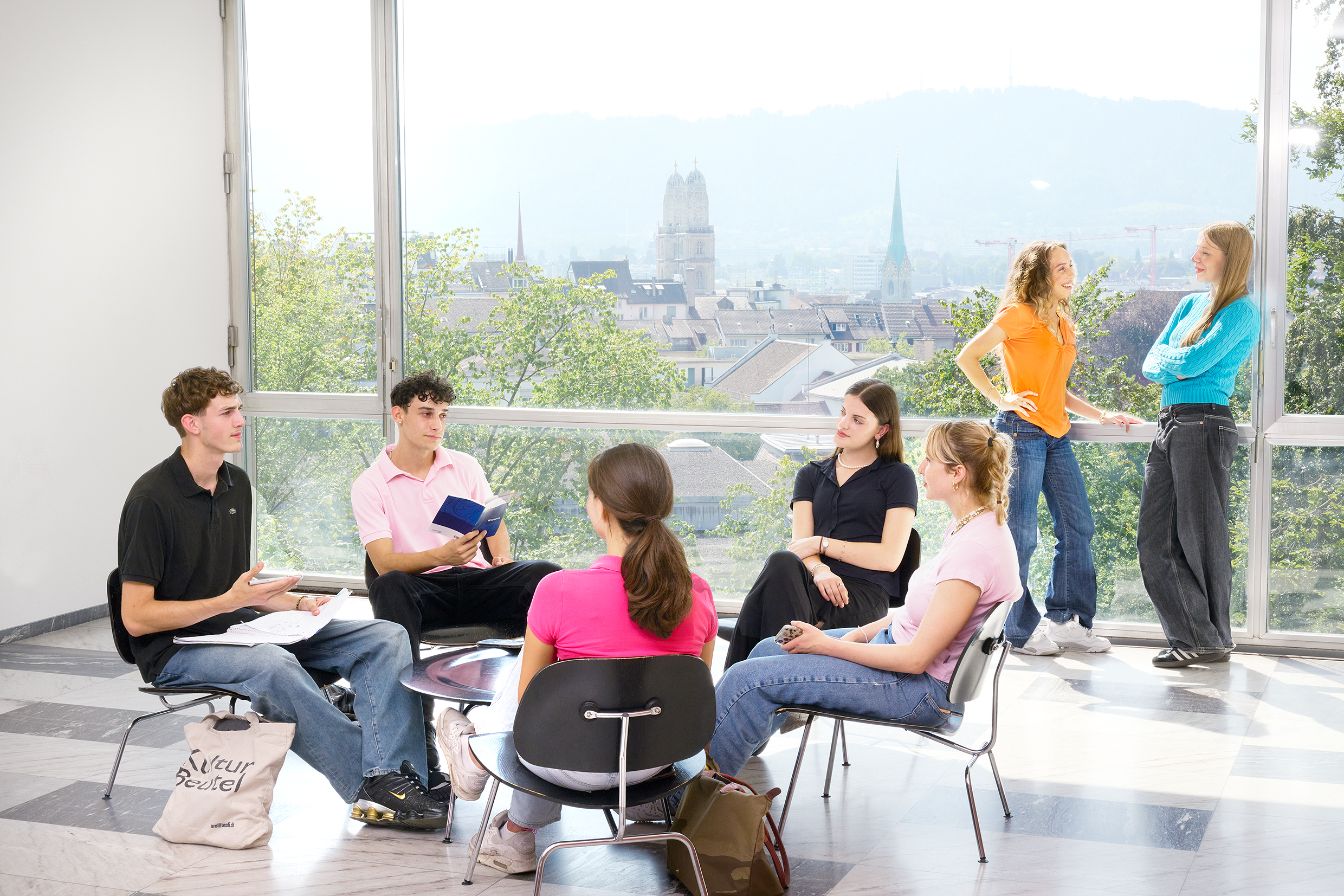 Studierende sitzen im kleinen Foyer im ersten Stock rund um einen Tisch - ins Gespräch vertieft.